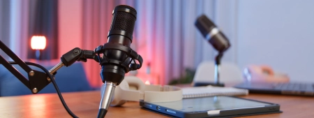 Home studio record equipment setup with microphones, headphones, digital tablet, laptop computer in neon lighting at night. Live streaming broadcast, podcast event preparation, online social media job