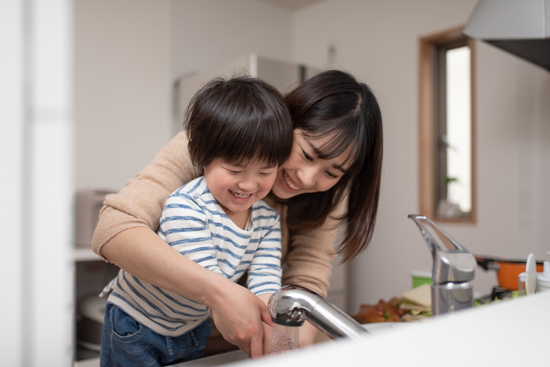 Mother teaches child how to wash hands in kitchen